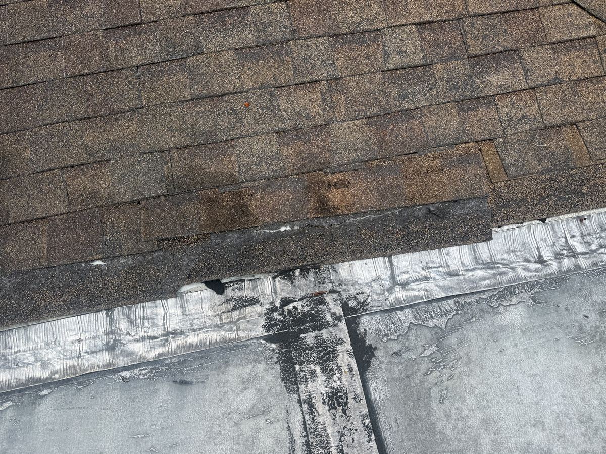 Loose, separated shingles at a shingle-to-flat roof transition